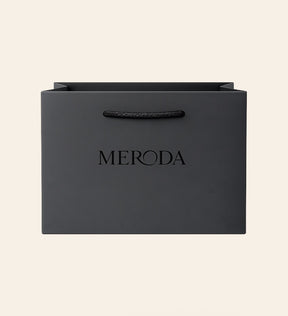 Gift Bag in matte black featuring a woven rope handle and embossed Meroda logo on a cream background.