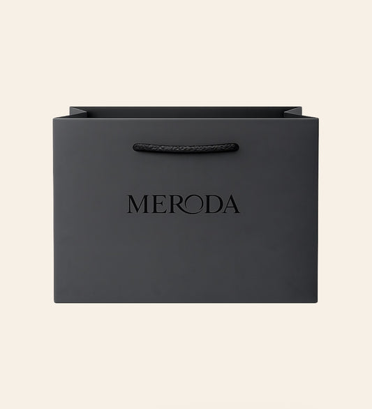 Gift Bag in matte black featuring a woven rope handle and embossed Meroda logo on a cream background.