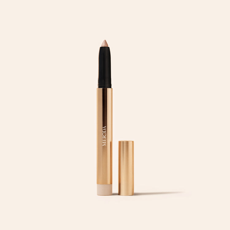 Eye Perfecting Shimmer Stick en Champagne con estuche dorado abierto y punta brillante sobre fondo crema.