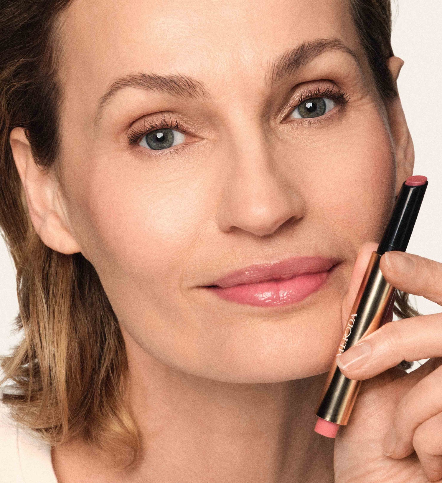 Model wearing the On The Go Bundle and holding the Hydrating Lip Tint in Dusty Rose for a natural, radiant look.